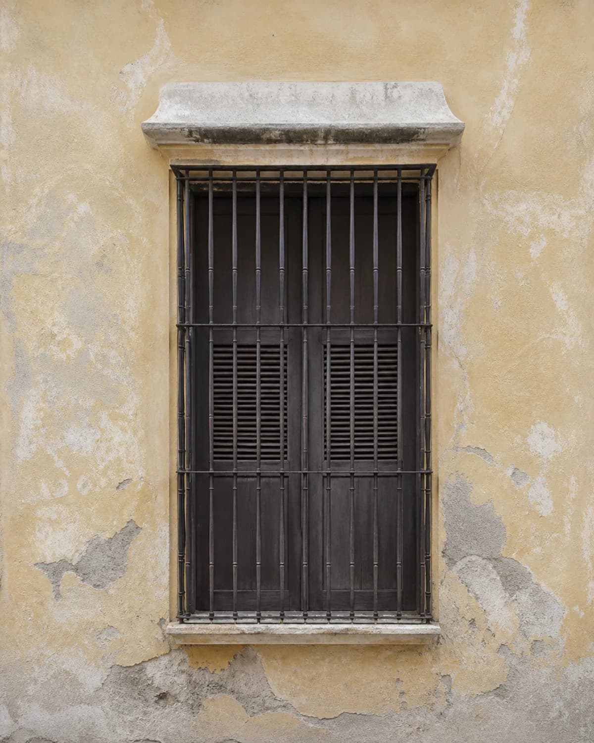 A shuttered window with a wrought-iron grille on a colonial facade in Santa Marta.