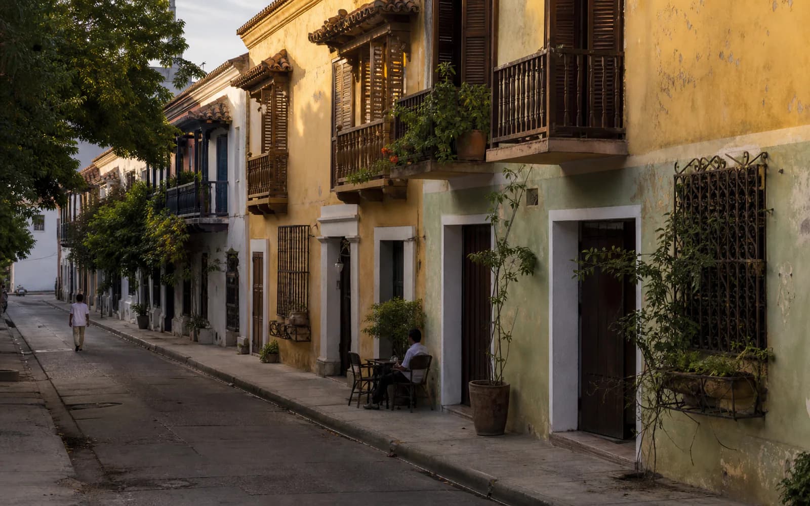 A street in the historic centre of Santa Marta in the afternoon, with plants, shade and people.